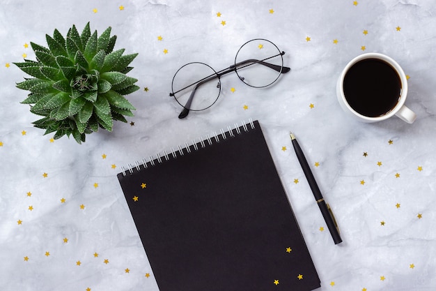 office or home table desk. black notepad, pen, cup of coffee, succulent on marble background