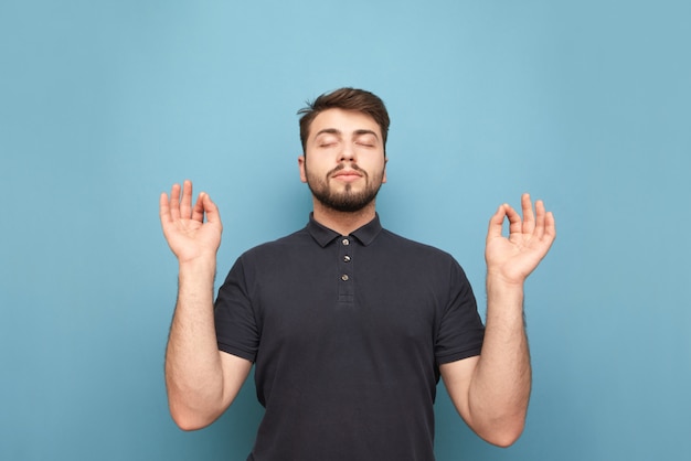 Офисный человек с бородой медитирует с закрытыми глазами и поднятыми руками