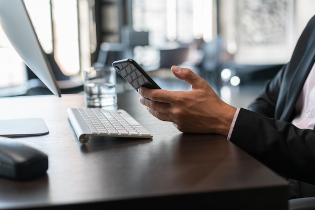 Office manager male hand holding a smartphone table with a computer keyboard closeup Businessman working in office with smartphone in hand concept of work