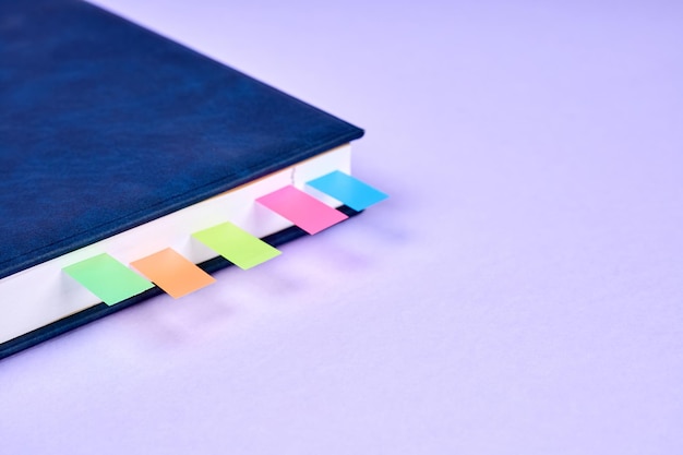 An office notepad with colorful sticky page markers sandwiched between pages on purple background