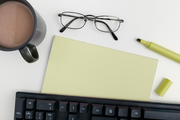 Office supplies over desk with keyboard and glasses and coffee\
cup for working remotely assorted school utilities for studying\
with hot drink and eyeglasses