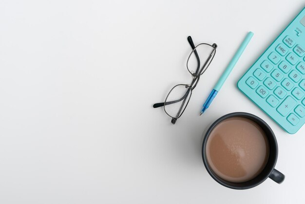 Office supplies over desk with keyboard and glasses and coffee\
cup for working remotely assorted school utilities for studying\
with hot drink and eyeglasses