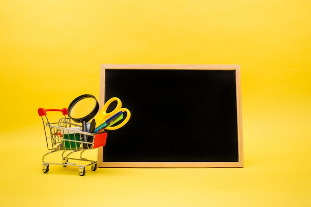 Office supplies in a metal cart and an empty slate on a yellow isolated with a copy of the space