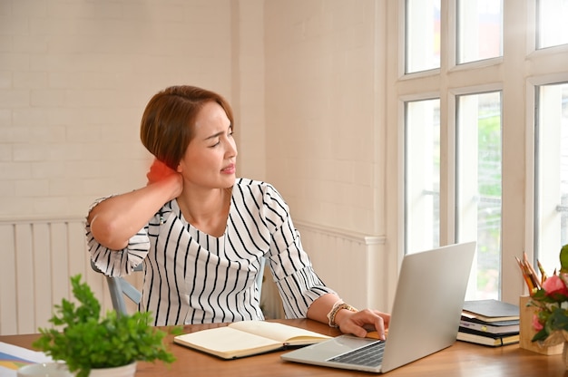 Office Syndrome, Woman touching massaging stiff neck to relieve pain in muscles working in incorrect bad posture.