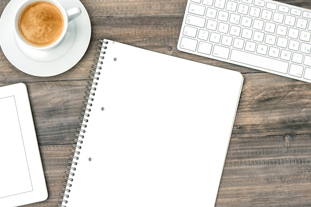 Office table flat lay. Digital tablet pc, keyboard and cup of coffee on wooden background