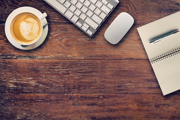 Office table with computer, notebook and coffee cup. View from above for vintage tone.