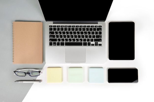 Office table with laptop computer, notebook, digital tablet and mobile phone on two tone b