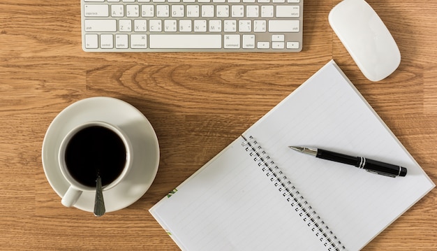 Office table with notepad, computer and coffee cup and computer mouse and pen