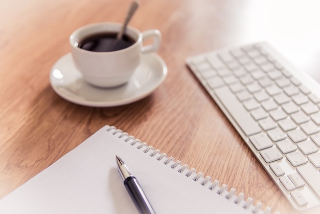 Office table with notepad, computer keyboard and coffee cup  and pen