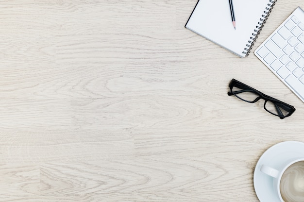 Office table with notepad, mouse, keyboard , coffee cup, black glasses. View from above with business flat lay design