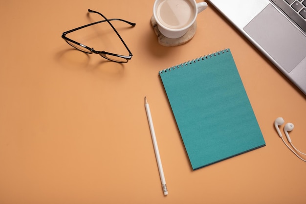 Office tafel bureau met set blanco blauw papier notitieblok beker potlood en laptop op gekleurde achtergrond Zakelijke of onderwijs werkruimte Bovenaanzicht