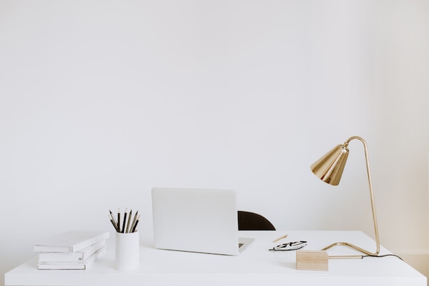 Office with laptop, lamp, notebooks. White work study cabinet workspace.