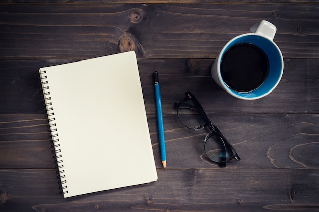 Office wood table with blank notepad, pencil, glasses and cup of coffee.