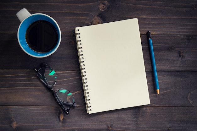 Office wood table with blank notepad, pencil, glasses and cup of coffee.