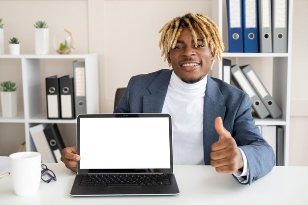 Office work Happy black man Online communication Handsome positive guy showing like gesture sitting desk opened laptop blank screen in light room interior