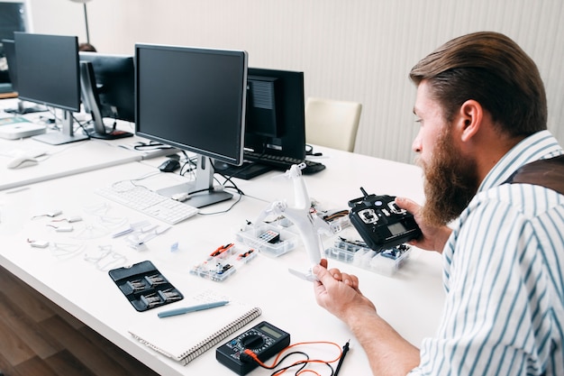 Office worker assembling drone at work. Bearded man sitting in open space with quadrocopter and tools, and constructing electronic toy