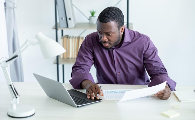 Office worker Busy man Important tasks Stylish guy purple shirt holding documents typing laptop in light room interior