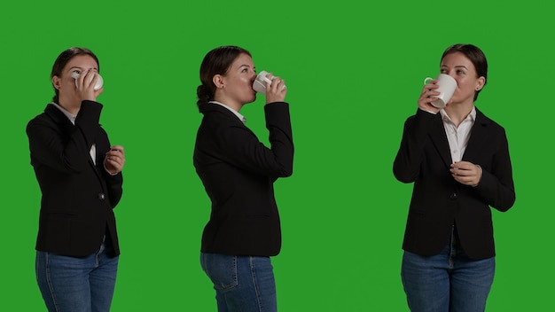 Office worker holding cup of coffee and drinking refreshment in studio, standing over isolated greenscreen. Corporate manager in suit serving caffeine beverage or drink, businesswoman.