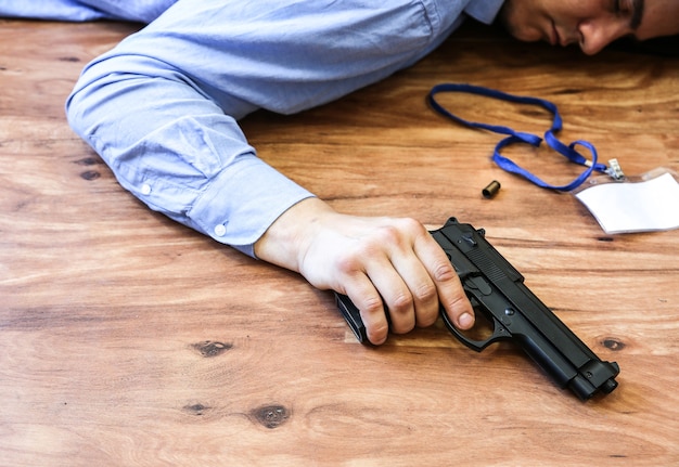 L'impiegato si trova sul pavimento tenendo la pistola in mano. suicidio per stress da lavoro. depressione o esaurimento. situazione di vita terribile. uomo vicino al computer portatile alla scrivania.