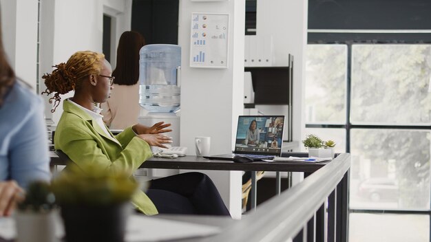 Office worker using online remote conference on webcam, talking to business people about development. Female employee chatting on videoconference call, videocall meeting in office.