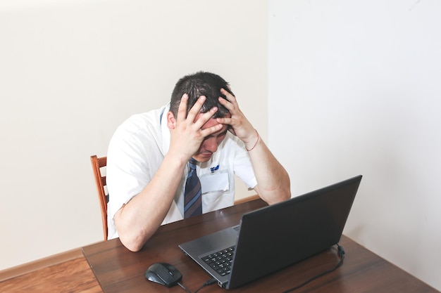 Office worker in white shirt. Occupational burnout. Bad work conditions. Unhappy manager with laptop. Summer heat. Meeting deadlines. Stressful job at the desk.