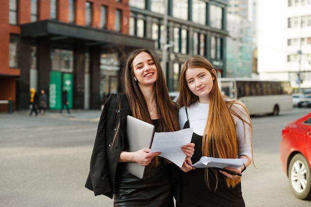 office workers standing on street with a laptop and business papers in hands and posing at camera