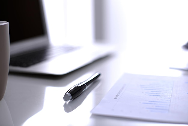 Office workplace with a laptop and financial documents on the light reflecting table