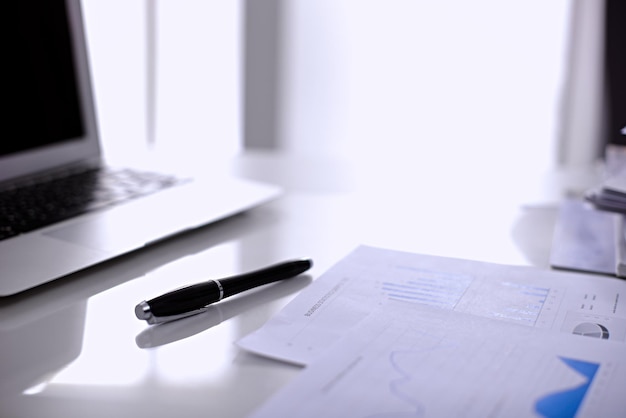 Office workplace with a laptop and financial documents on the light reflecting table