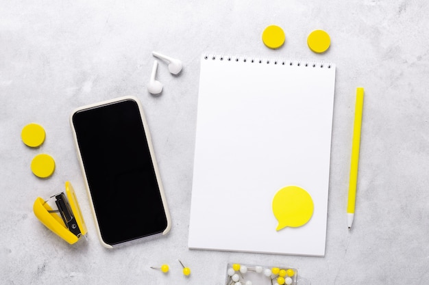 Ufficio di lavoro con smartphone, blocco note e accessori di cancelleria su sfondo grigio pietra. illuminating yellow e ultimate grey, i colori dell'anno 2021