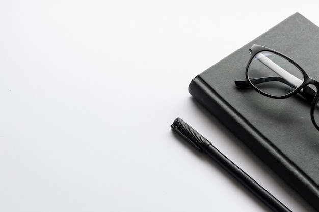 Office workplace with text space, black book and spectacles on white table 