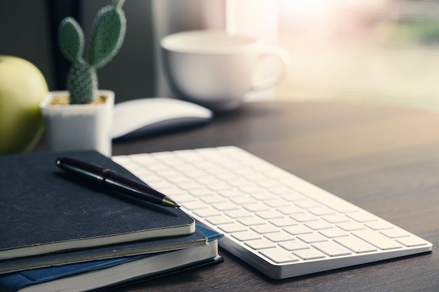 Area di lavoro dell'ufficio con la tastiera e i rifornimenti di computer sopra sopra la tavola di legno leggera.