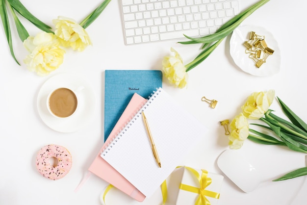 Office workspace with a white desk Top view from above with a keyboard notepad gift flowers and pencil with a white cup of coffee on a plate Flat surface with copy space Women's business concept