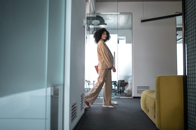 In the office .Young woman in beige suit walking in the office corridor