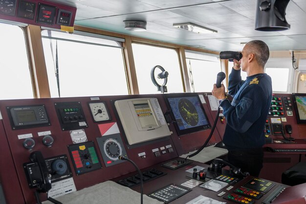 Фото Офицер на страже с радио на навигационном мостике кавказский мужчина в синем униформе свитере на мостике грузового корабля