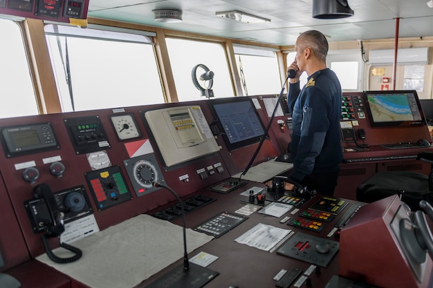 Officer on watch with radio on the navigational bridge Caucasian man in blue uniform sweater on the bridge of cargo ship