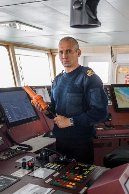 Ufficiale di guardia con sart sul ponte di navigazione uomo caucasico in maglione uniforme blu che utilizza il transponder radar di ricerca e salvataggio sul ponte della nave da carico