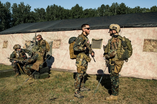 Officer with rifle preparing soldier for military operation and giving advice to him at military base