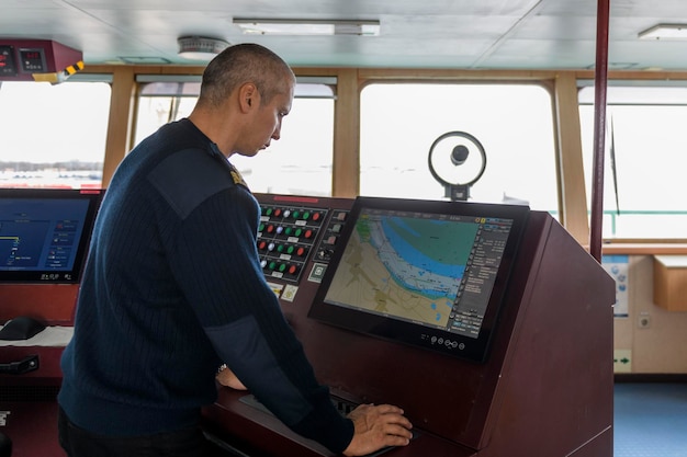 Officier op wacht met elektronische kaart op de navigatiebrug blanke man in blauwe uniform trui met ECDIS op de brug van vrachtschip