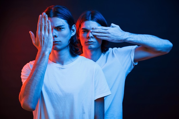 Ogen bedekken met handen. Portret van tweelingbroers. Studio-opname in donkere studio met neonlicht.