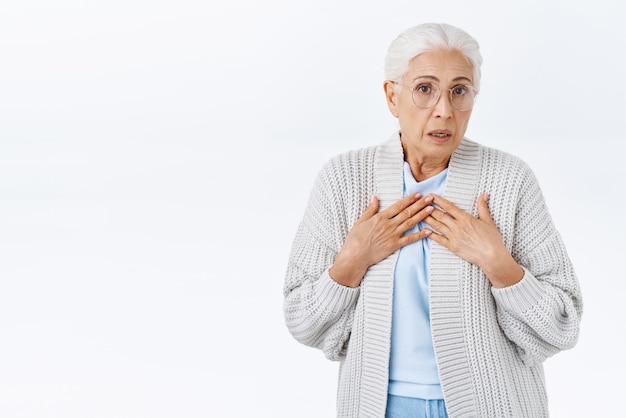 Oh dear Concerned senior lady with grey hair in glasses and warm cardigan looking overwhelmed and shocked press hands to chest exhale nervously and stare camera shocked heard troublesome news