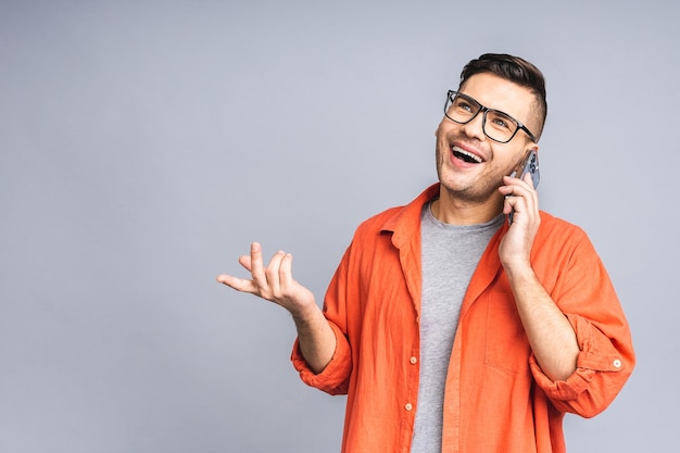 Oh geweldig nieuws glimlachende jonge casual man in glazen praten op de mobiele telefoon geïsoleerd over witte grijze achtergrond