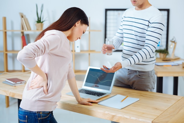 Oh my back. Yong office worker bowing her head and touching her back while suffering pain