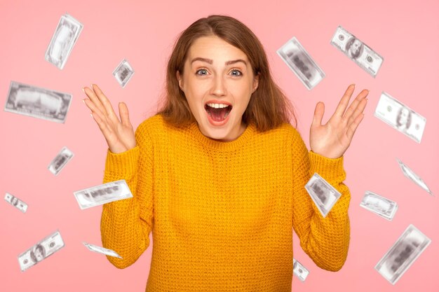 Oh my god wow portrait of amazed young woman looking at camera\
with big eyes absolutely shocked of money rain falling from up\
indoor isolated on pink background