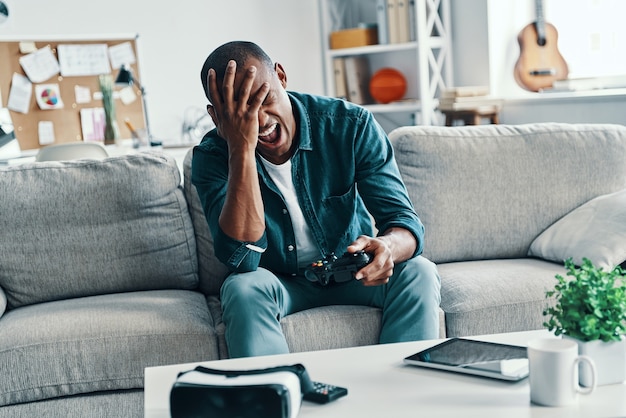 Oh no! Disappointed young African man covering face with hand while sitting on the sofa at home