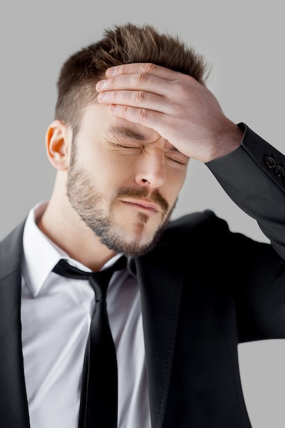 안 돼! 회색 배경에 서 있는 동안 머리에 손을 잡고 눈을 감고 있는 정장을 입은 좌절한 젊은 남자의 초상화