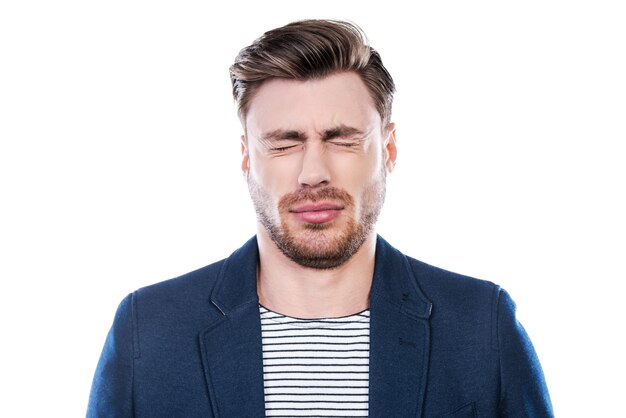 Oh no! Portrait of young man expressing negativity and keeping eyes closed while standing against white background