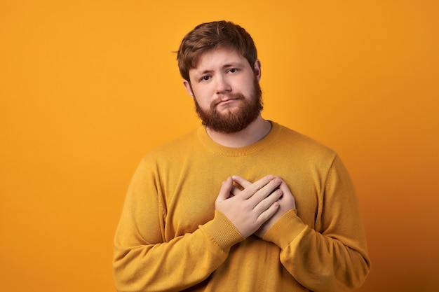 Oh, thank you very much Attractive unshaven young male keeps hands on heart, expresses gratitude, stands against white studio wall