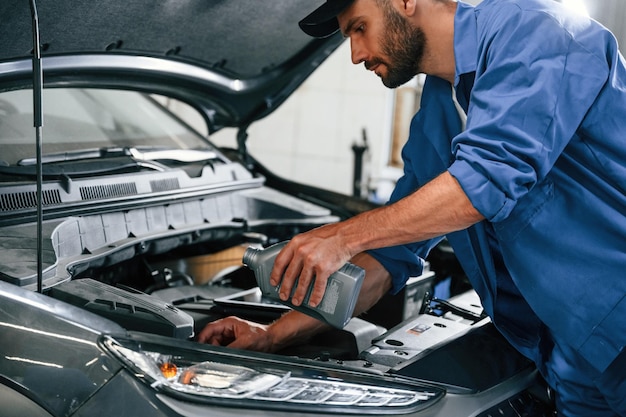 Photo oil can in hands auto mechanic working in garage repair service