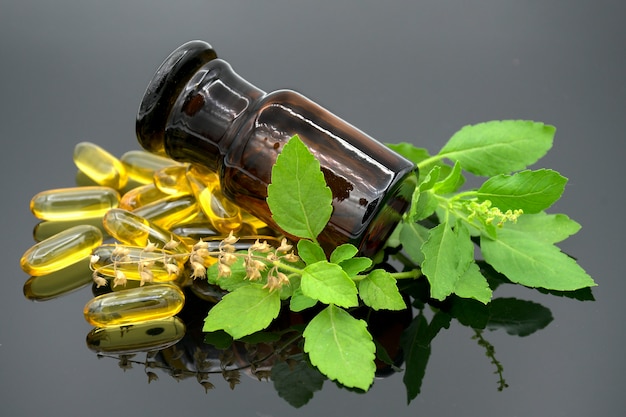 Oil in capsule, amber bottle and fresh herbs on dark background.