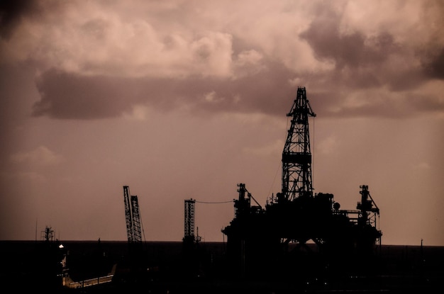 Foto siluetta dell'impianto di perforazione di trivellazione petrolifera sopra un cielo nuvoloso